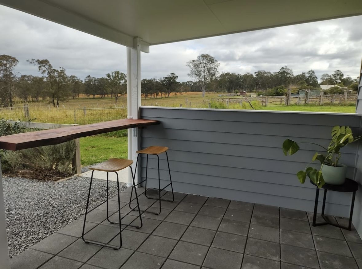 Covered outdoor deck with a timber bar and stools looking across the farm