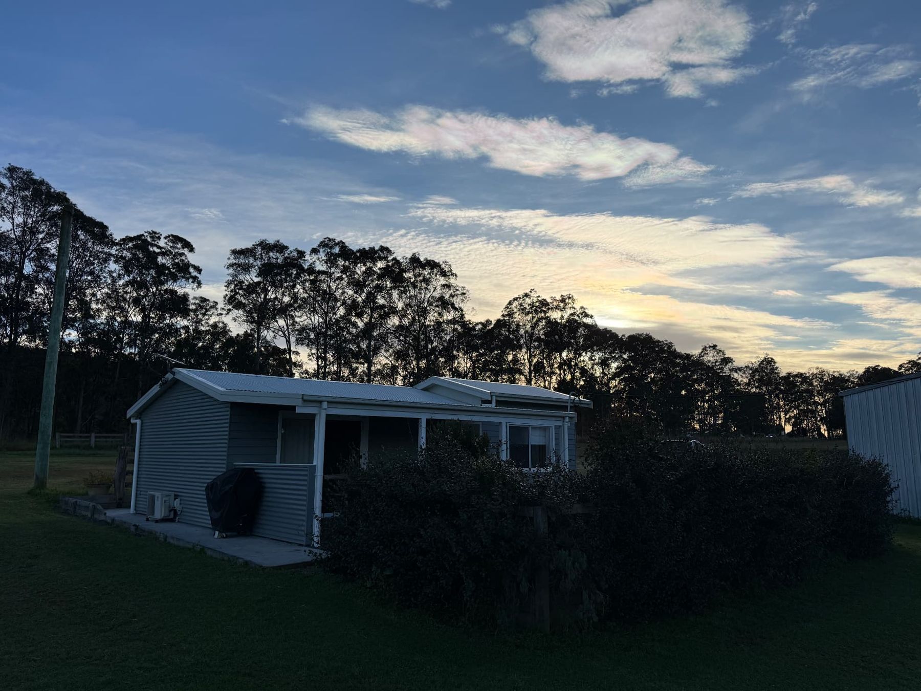 Baroona Dairy Farm Cottage at dusk with the paddocks and hills behind it, Nabiac NSW